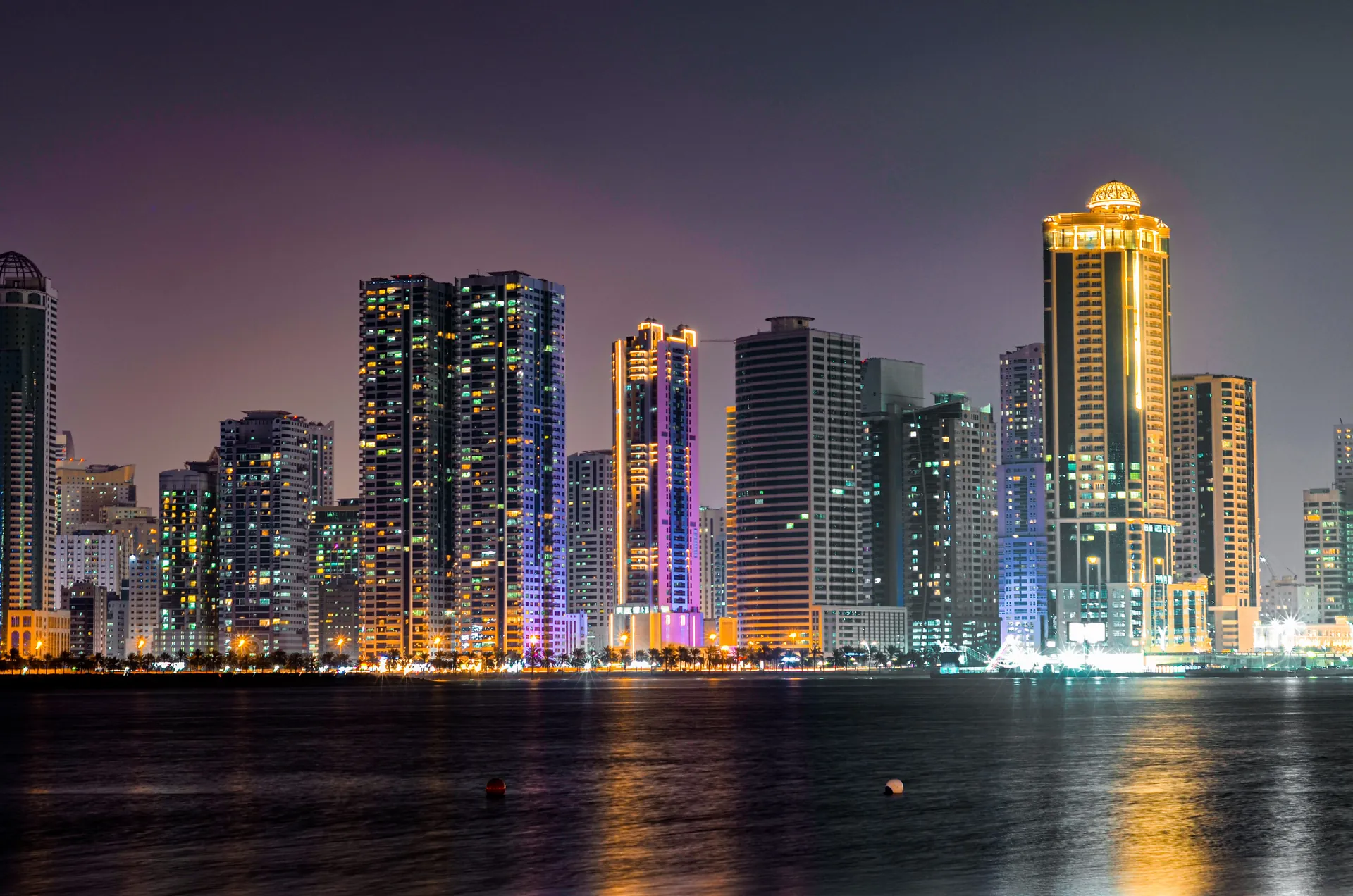 Illuminated Sharjah waterfront towers reflected in the lagoon at night
