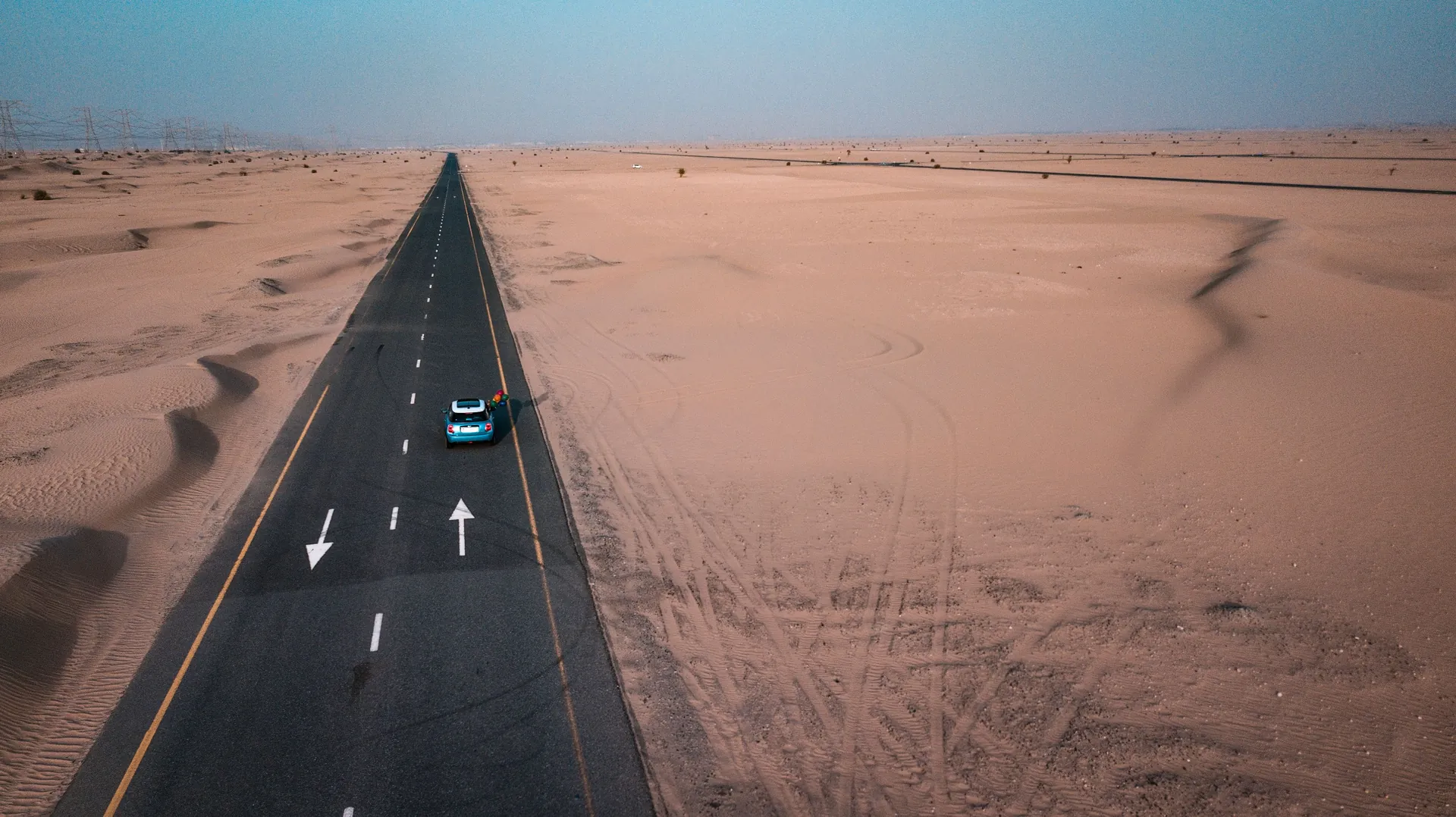 A car on a paved road through desert dunes